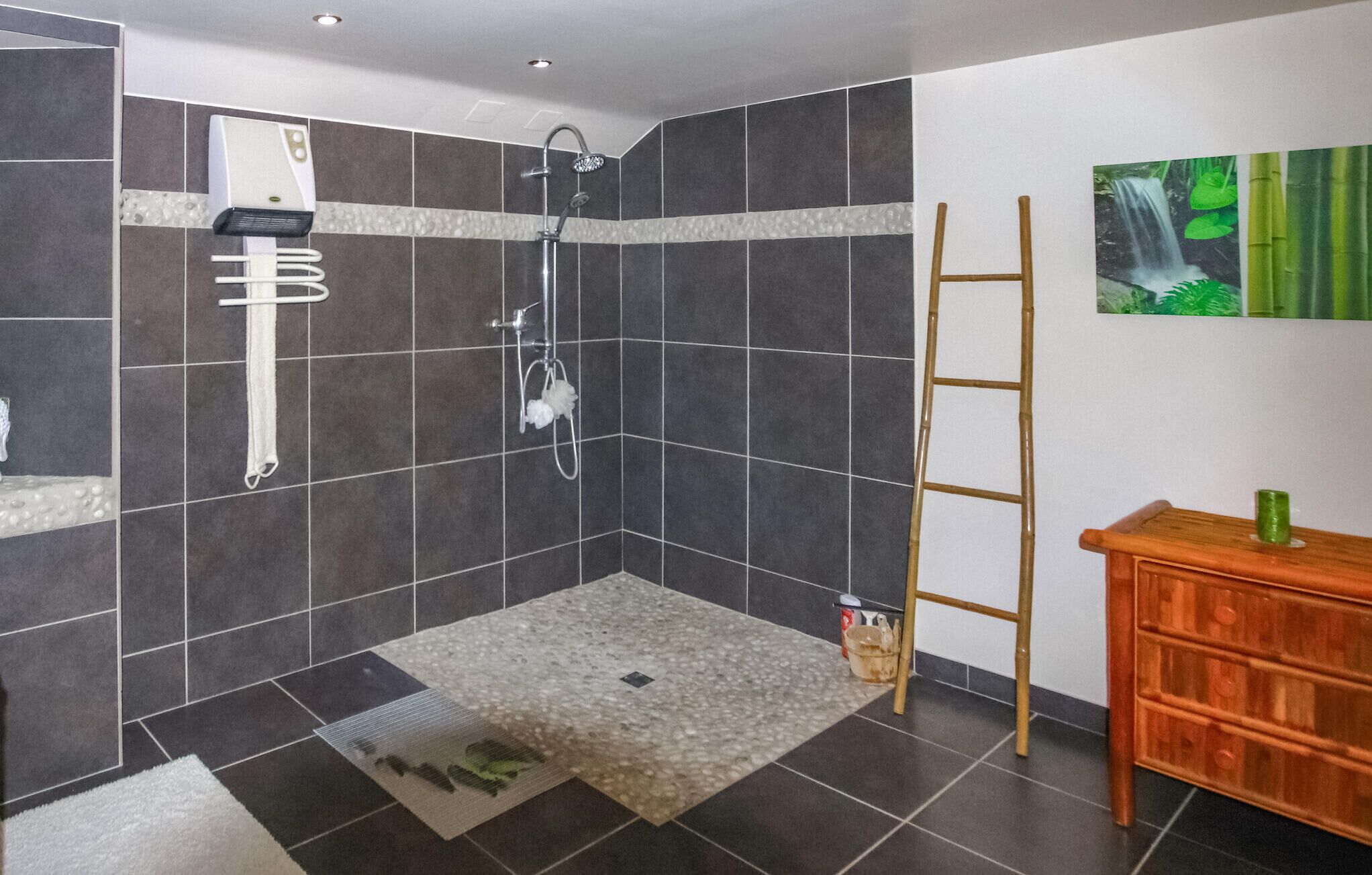 Un espacio de ducha con azulejos oscuros, un perchero blanco, un cabezal de ducha y una escalera de madera.