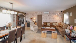Ein Wohnzimmer mit Steinwand, einer Essecke mit Tisch und Stühlen sowie einer Couch mit Kissen.