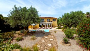 Eine gelbe Villa mit Pool, umgeben von Olivenbäumen und einem Schotterweg.