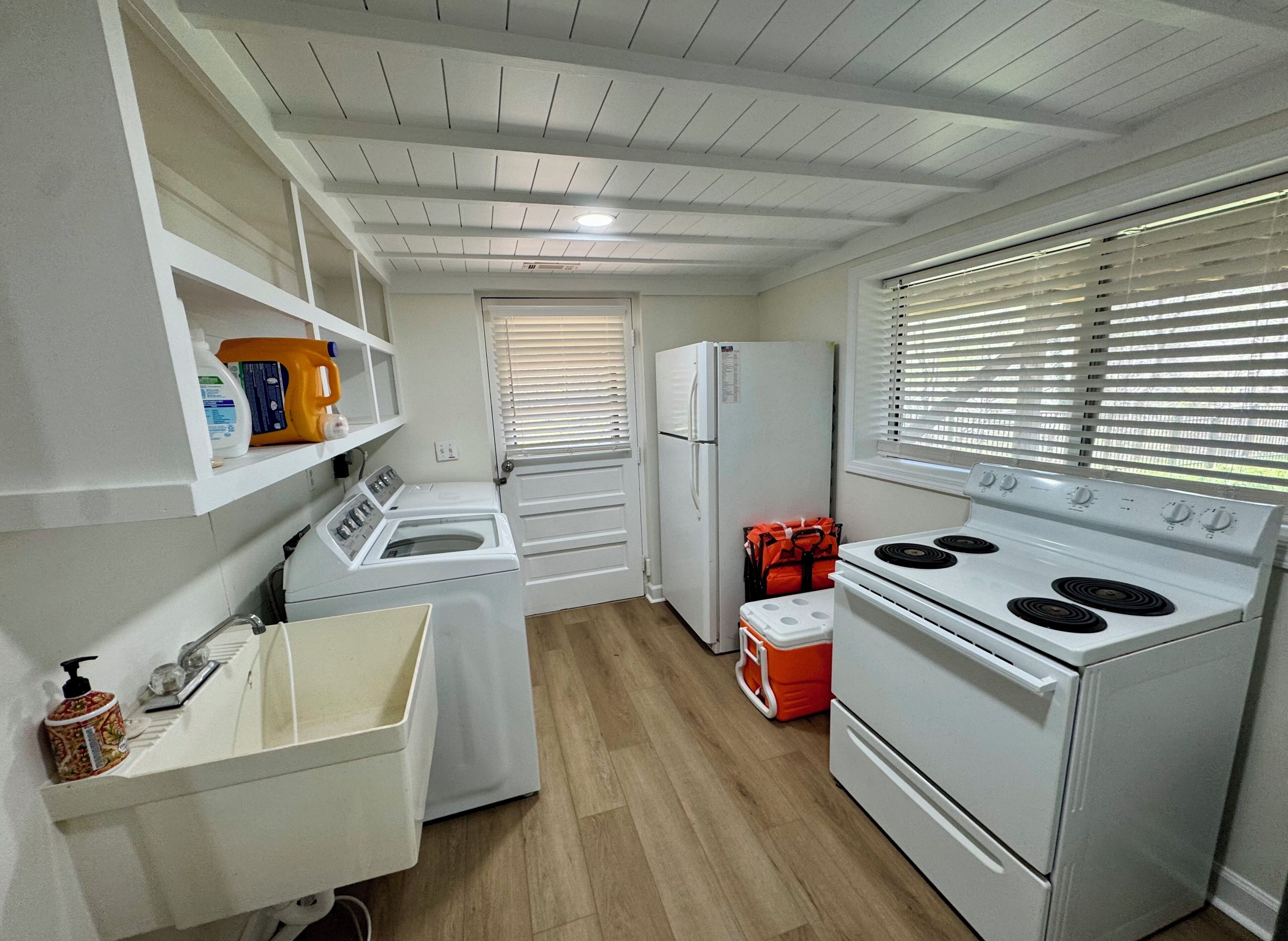 Une cuisine compacte équipée d’un lave-linge, d’un réfrigérateur, d’une cuisinière et d’une fenêtre avec des stores.