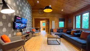Un intérieur de chalet chaleureux avec un téléviseur, des meubles en bois et de grandes fenêtres.