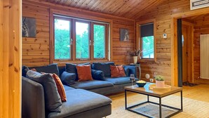Un intérieur de chalet chaleureux avec un grand canapé d’angle gris, une table basse en bois et un panneau indiquant une « salle Champagne ».