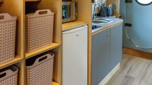 A compact kitchenette with a built-in fridge, a sink, and wooden shelves with storage baskets.