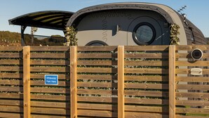 A wooden fence with a sign reading "Whitewisp Park Here" and a large structure with a circular window and barbed wire.