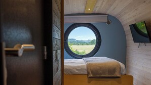 A compact bedroom with a single bed, a round window, and a wooden ceiling.
