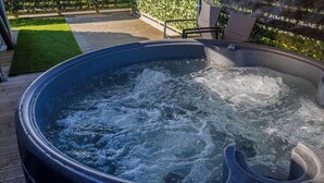 A hot tub with water bubbling, surrounded by a wooden deck and a green hedge.