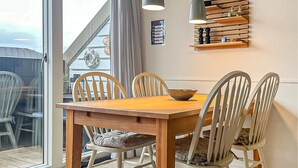 Et spiseområde med et træbord og fire stole, en skål på bordet, samt en vægmonteret hylde med dekorative genstande.