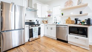 A modern kitchen with stainless steel appliances, white cabinetry, and wooden flooring.
