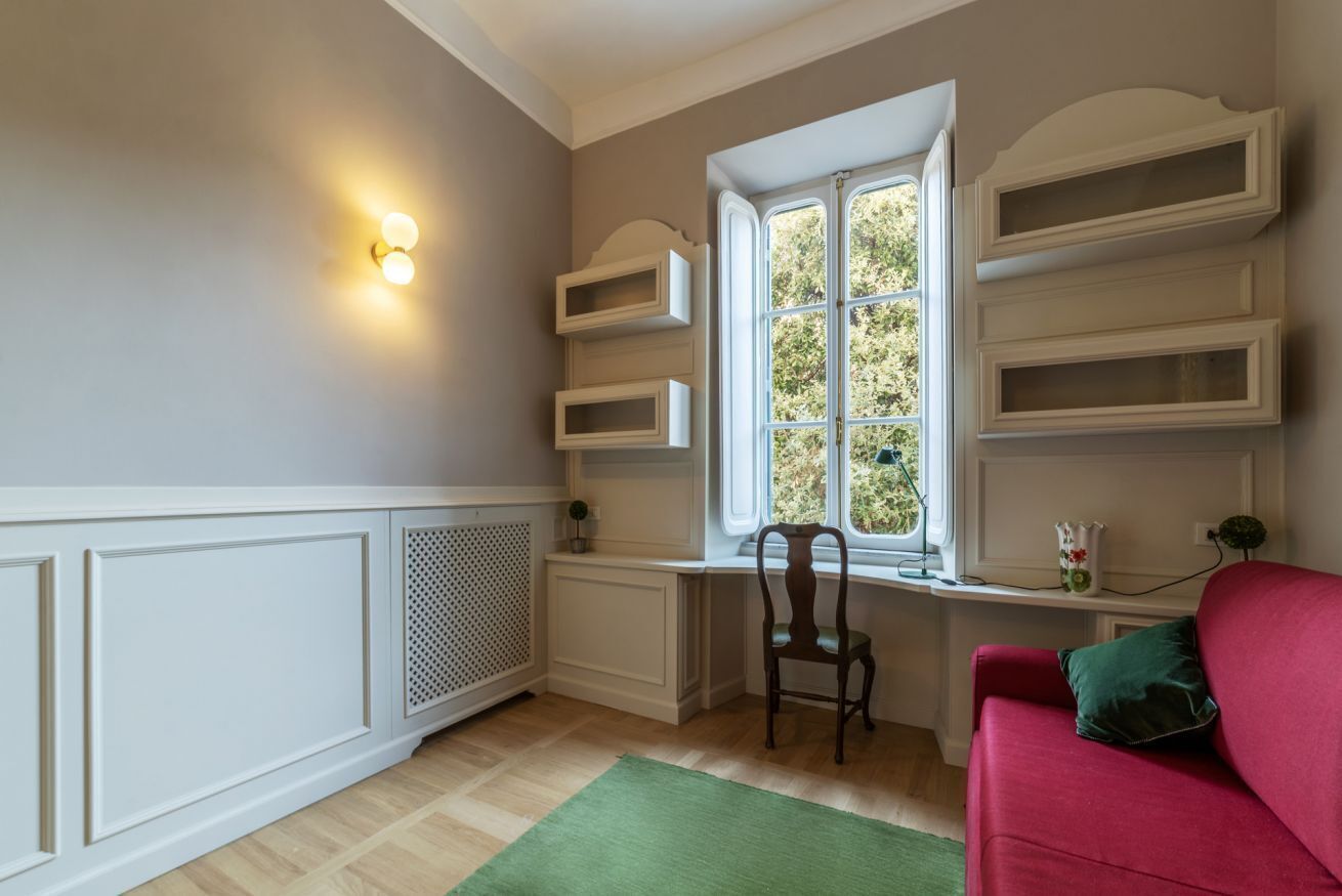 Ein Zimmer mit integriertem Schreibtisch, einem roten Sofa, einem Fenster mit Regalen und einer Heizung.