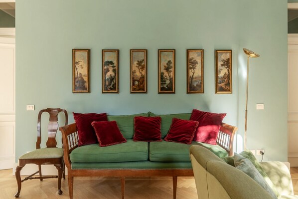 A living room with a green sofa, red cushions, a wooden chair, and a floor lamp.