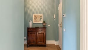 Een gang met een houten kast, een ingelijst botanisch kunstwerk en een hangende lamp.