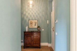 A hallway with a wooden cabinet, a framed botanical print, and a hanging light fixture.
