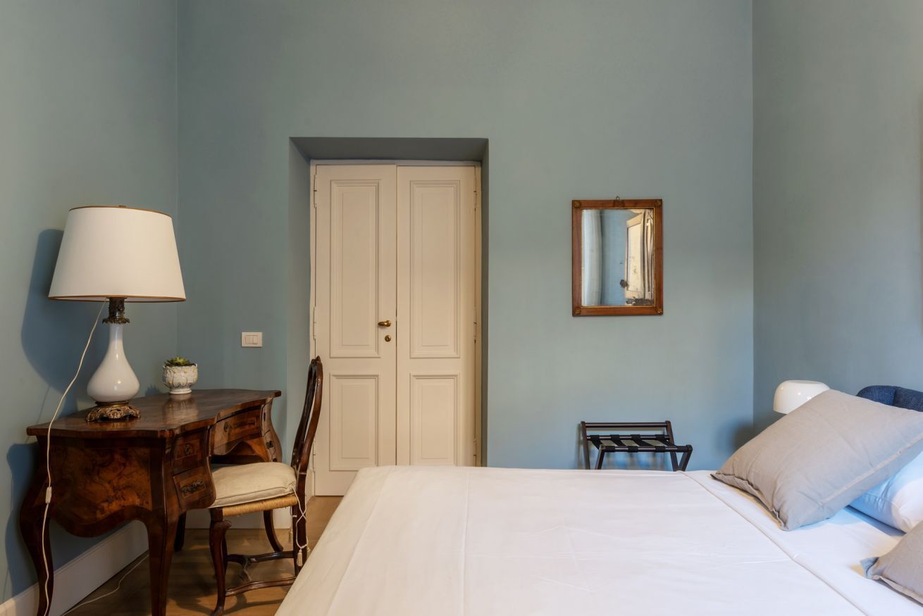 A bedroom with a bed, a desk, a chair, a wardrobe, and a mirror.