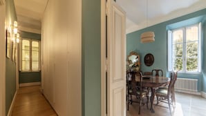 Een eethoek met een houten tafel en stoelen, een kroonluchter en een raam met uitzicht op bomen.