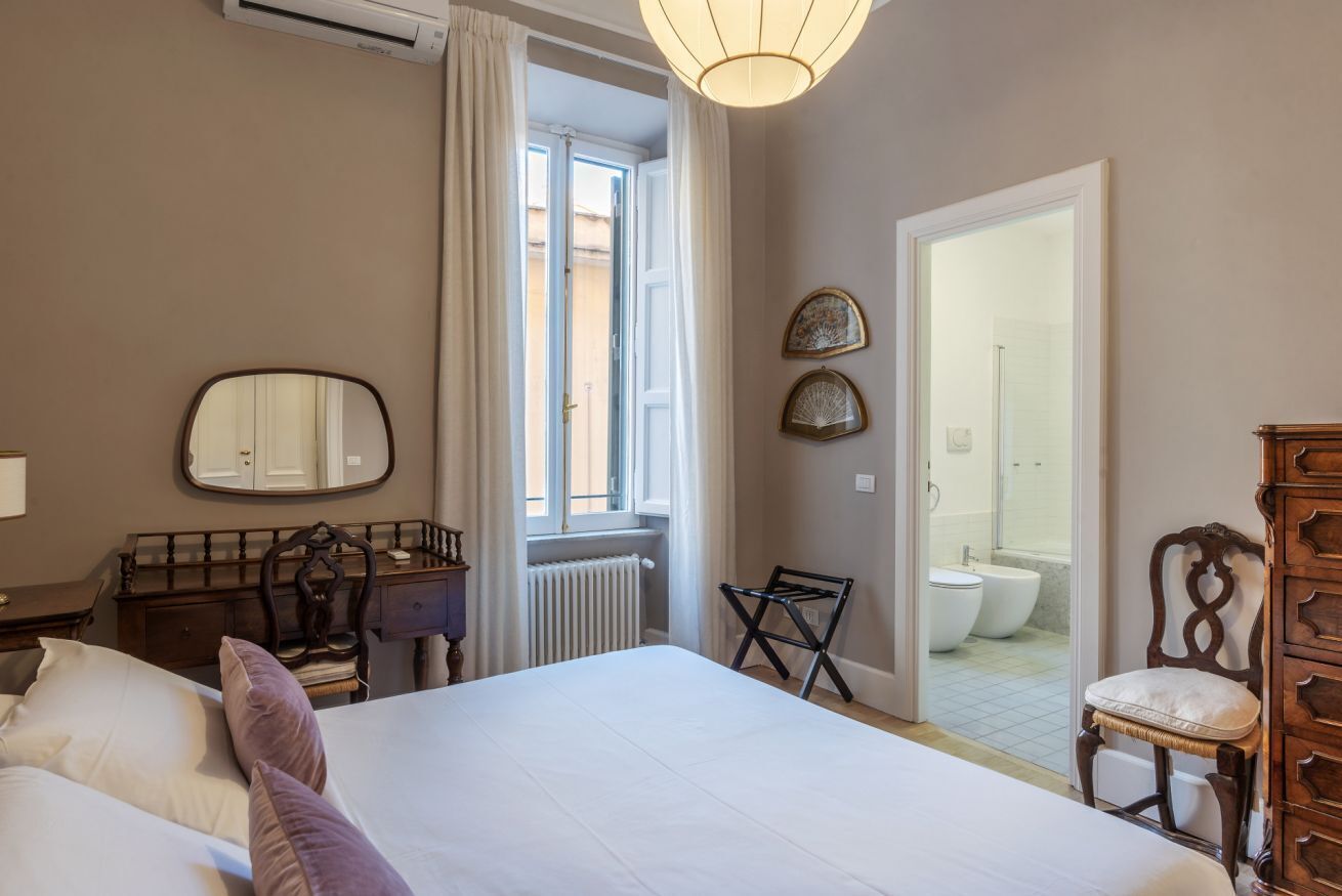 A bedroom with a bed, a dresser, a mirror, and a view of a bathroom with a toilet and a bathtub.