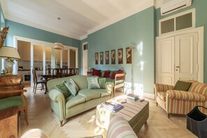 A living room with a sofa, armchair, and a coffee table. There is a dining table with chairs and a lamp.