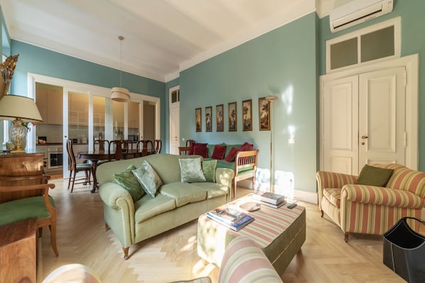 A living room with a sofa, armchair, and a coffee table. There is a dining table with chairs and a lamp.