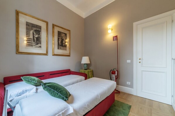 A room with two beds, a fire extinguisher, a door, and framed pictures on the wall.