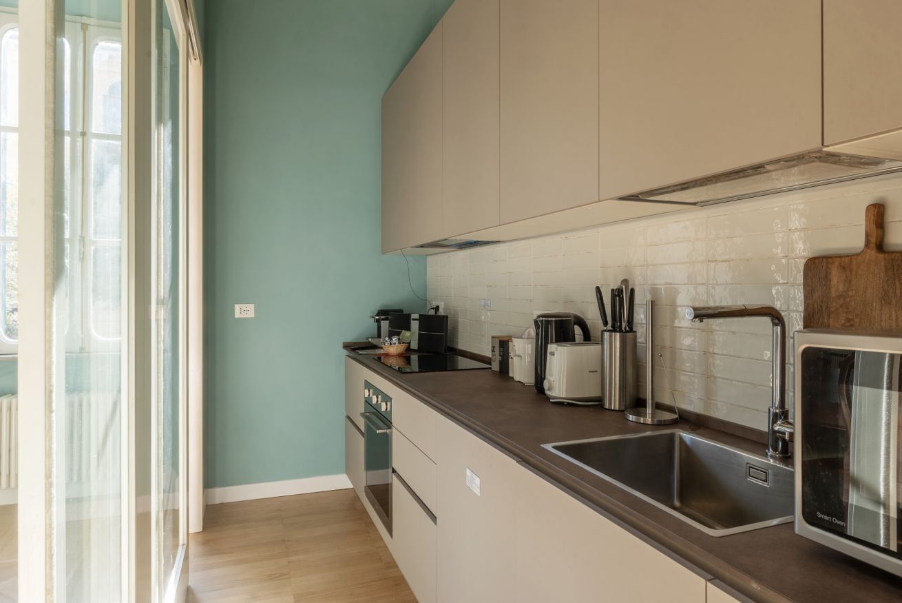Una cocina moderna con horno integrado, un lavamanos y ventana con vistas a un jardín.