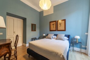 A bedroom with a large bed, a wooden desk, a chair, and two wall-mounted lamps.