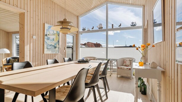 A dining area with a wooden table and chairs, large windows with views of ships, and a hanging light fixture. - 2 bedroom gorgeous home in Juelsminde (Juelsminde)