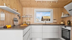 A modern kitchen with wooden walls, white cabinets, and a large window overlooking a snowy landscape. - 2 bedroom gorgeous home in Juelsminde (Juelsminde)