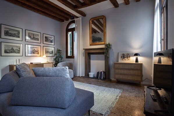 Una sala de estar con sofá, chimenea, cuadros enmarcados y televisor.