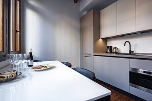 A modern kitchen with a white countertop, stainless steel appliances, and a dining area with a white table and chairs. - Ca' Vida Piano Nobile (Venezia)