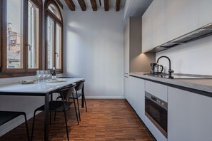 A compact kitchen with a dining table, chairs, a built-in oven, and a window with a view of buildings.