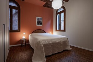 A bedroom with a large bed, wooden flooring, two windows, a picture on the wall, and a bedside lamp. - Ca' Vida Piano Nobile (Venezia)