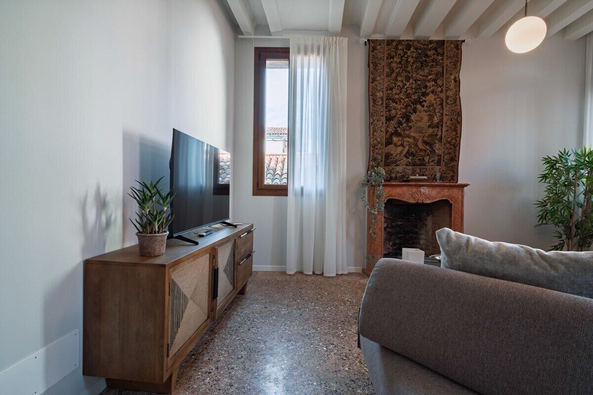 A modern living room with a television, sofa, fireplace, and potted plants.