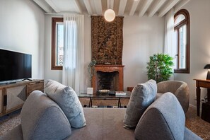A modern living room with a fireplace, two grey sofas, a flat-screen TV, and a large window.