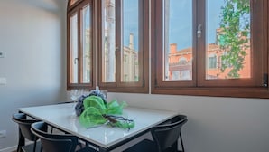A dining area with a table and chairs, a window with a view of buildings, and a plant on the table. - Ca' Vida Trifora (Venezia)