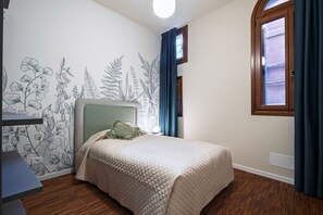 Un dormitorio con cama, escritorio, ventana y pared con un mural botánico.