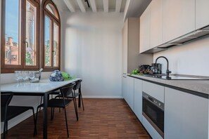 Cocina compacta con comedor, ventanas amplias y vista a edificios.