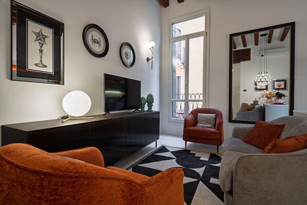 A living room with a black entertainment unit, a television, orange and grey sofas, a black and white rug, and a large mirror.