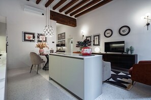 A modern kitchen with a central island, a dining area with chairs, a TV, and framed pictures on the wall.