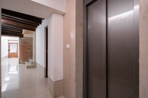 A hallway with a modern elevator, a door, and a staircase leading to a brick wall.