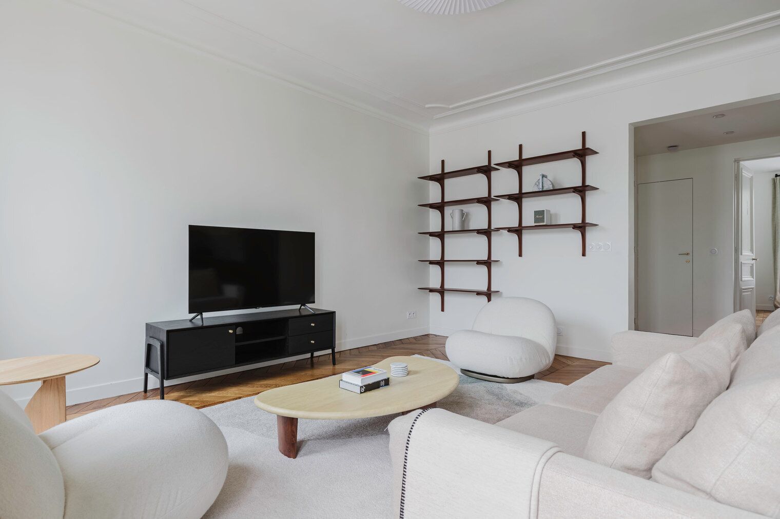 A modern living room with a flat-screen TV, a sofa, a coffee table, and a wooden shelving unit.