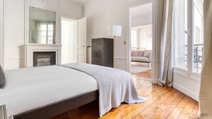 Un dormitorio con cama, cómoda, espejo y vistas a un salón a través de una puerta abierta.