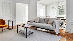 Una sala de estar con un sofá gris, una mesita de centro, una silla y una lámpara colgante.
