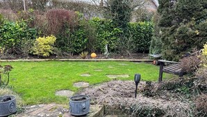 Un jardín con césped, piedras para caminar y un banco.