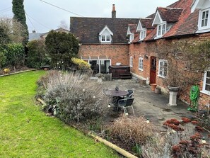 Une maison en briques avec un patio et un jardin, une table ronde et des chaises.
