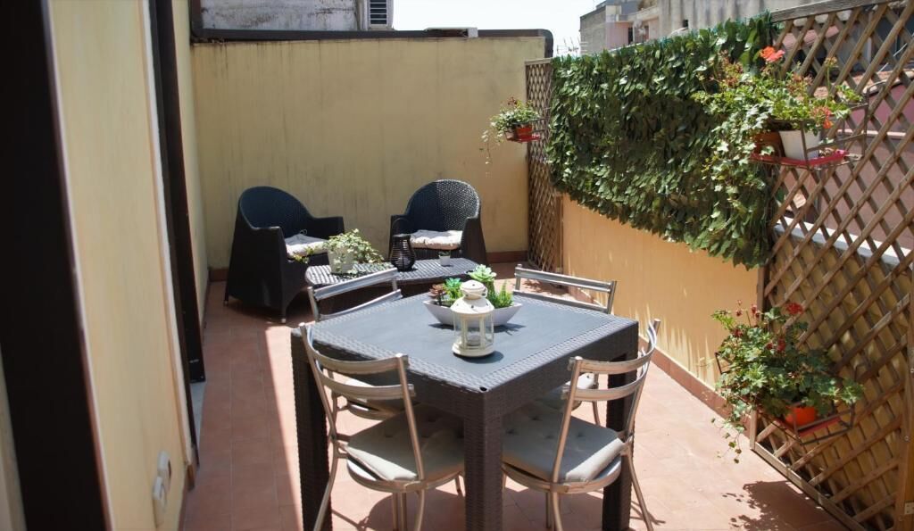 An outdoor patio with a table and chairs, surrounded by a wooden fence and potted plants.
