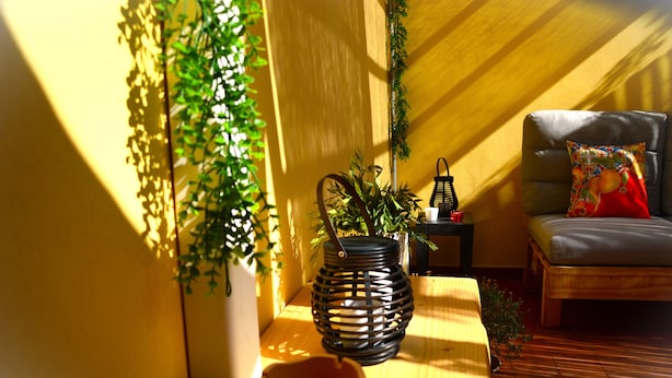 A cozy room with a wooden floor, a small table with a potted plant, a candle, and a chair with a colorful cushion. - Case Vacanze Il Sorriso (Catania)