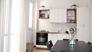 A kitchen with white cabinets, a microwave, a stove, and a dining table with chairs. - Case Vacanze Il Sorriso (Catania)