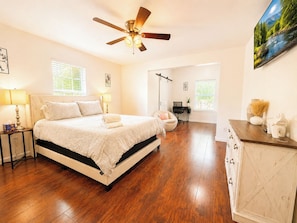 A bedroom with a bed, bedside tables, a desk, a chair, a ceiling fan, and a painting on the wall. - Spacious 3BR Family-Friendly, Big Yard, Game Table Near I-35 (Austin)