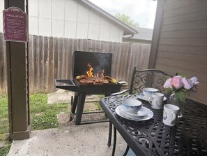 A backyard with a grill, a table with cups and a vase of flowers, and a sign with grill rules.