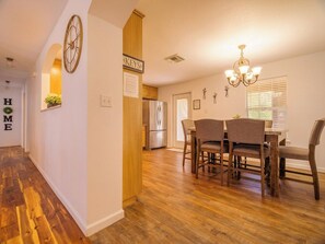 A modern kitchen with wooden flooring, a dining area with chairs, a clock, and a chandelier. - Spacious 3BR Family-Friendly, Big Yard, Game Table Near I-35 (Austin)