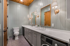 Ein Badezimmer mit einem weißen Waschbecken, zwei Spiegeln, einer Toilette und einer Waschmaschine.